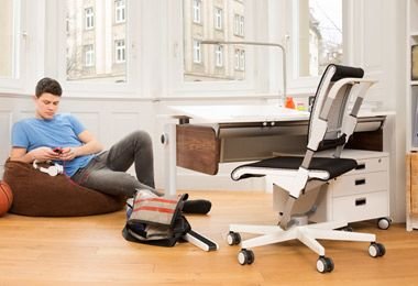 une chambre d'adolescent avec un bureau, une chaise et un caisson